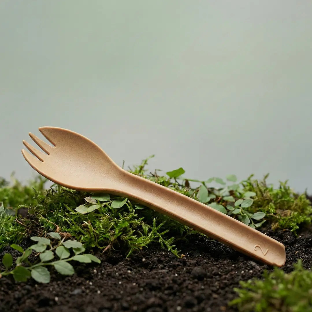 CompostEase | Spork placed on soil and moss outdoors, symbolizing compostable plant-fiber cutlery and environmental sustainability.