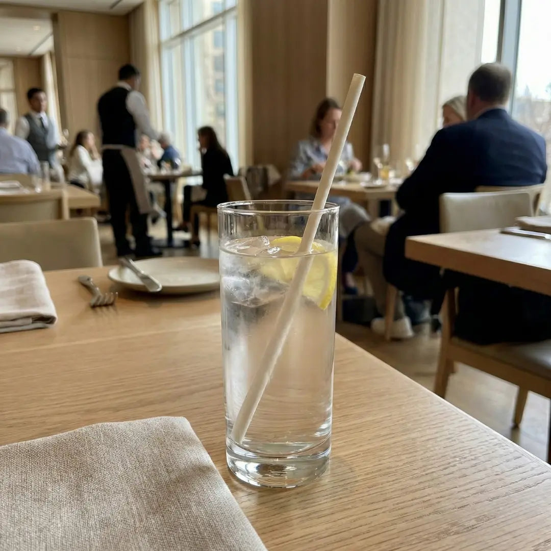 CompostEase 6mm molded fiber straw in a water glass with lemon, displayed in an upscale restaurant environment.