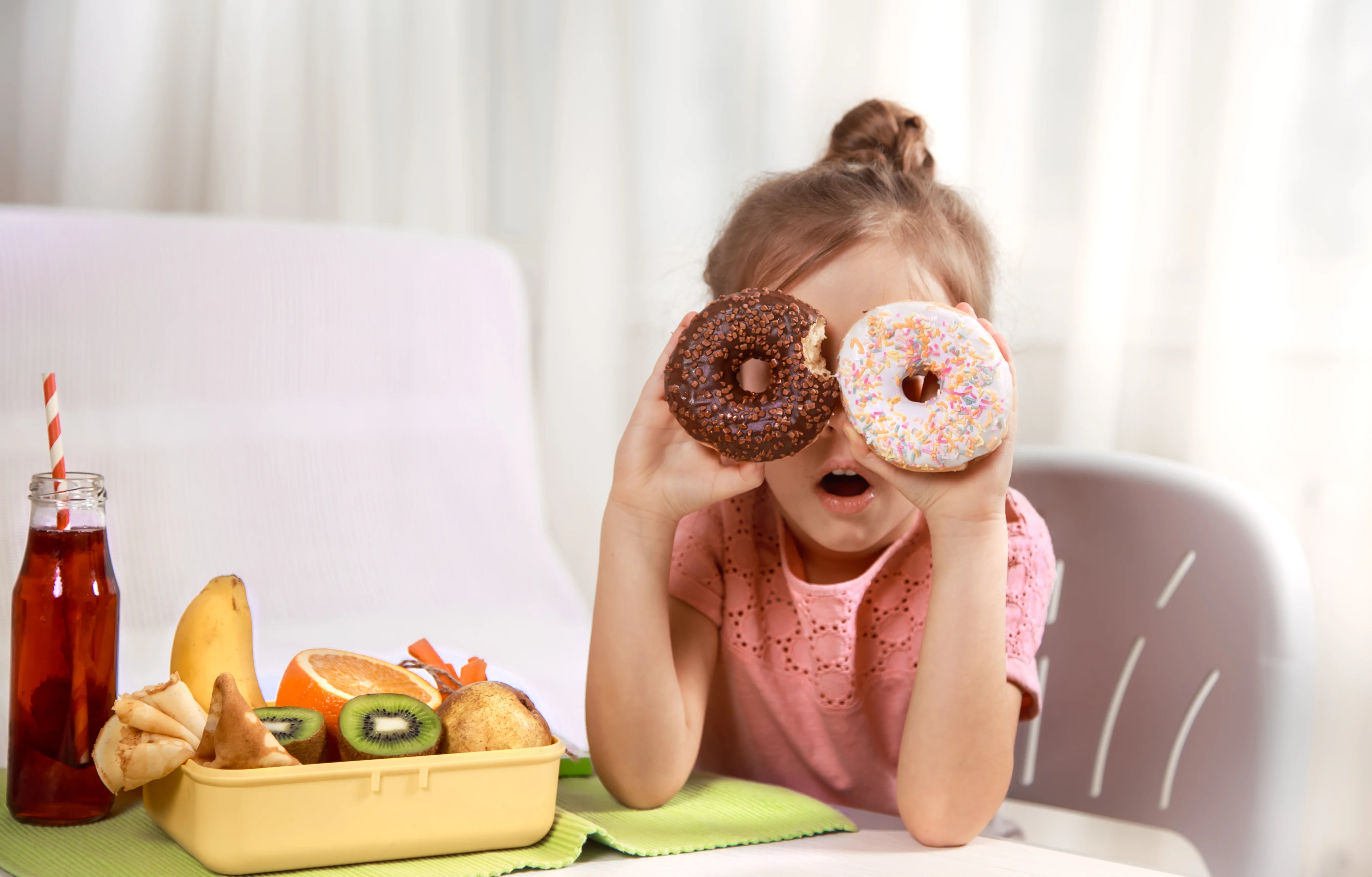 Child resistant packaging helps keep food safe—young girl playing with donuts at a table with a lunchbox filled with fresh fruits and juice.